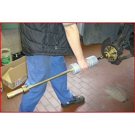 Ein Mechaniker benutzt ein Spezialwerkzeug, um ein Autoteil zu bearbeiten. Er steht in einer Werkstatt.